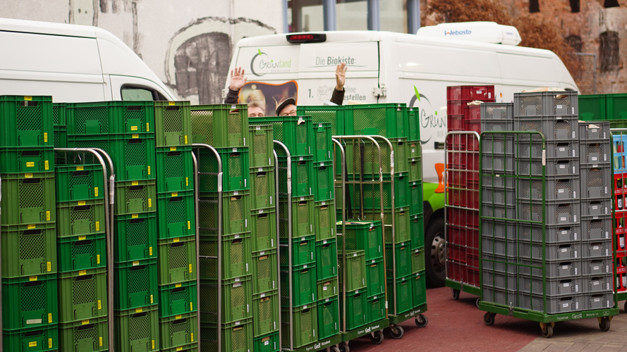 Rollwägen mit Grünen Kisten vor Lieferfahrzeugen