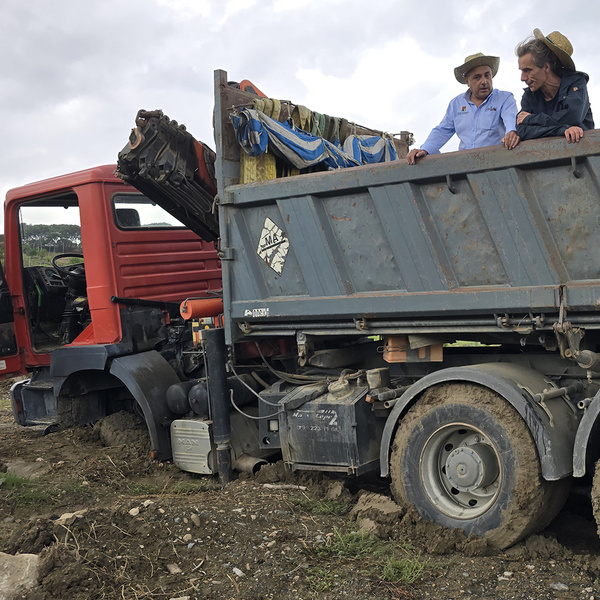 KI generiert: Ein LKW steckt im Schlamm fest, und zwei Personen mit Hüten stehen auf der Ladefläche und schauen sich die Situation an. Der Hauptinhalt des Bildes ist das festsitzende Fahrzeug und die Menschen, die es begutachten.