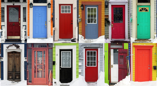 Das Bild zeigt eine Sammlung bunter Türen an verschiedenen Häuserfronten, umgeben von Schnee. Jede Tür hat eine einzigartige Farbe und Gestaltung.