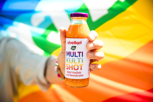 Hand hält Multi-Kuli-Shot, Regenbogenflagge im HIntergrund