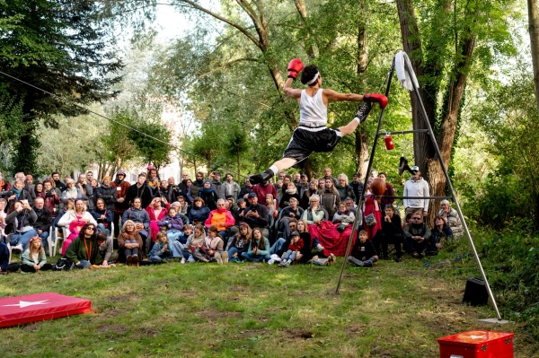 KI generiert: Eine Person in Boxkleidung führt einen Sprungtrick auf, Zuschauer schauen im Freien zu.