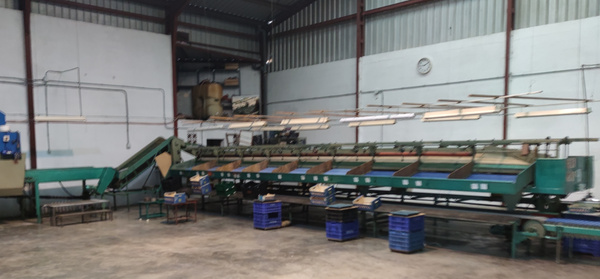 KI generiert: Das Bild zeigt eine industrielle Anlage in einem leeren Lagerhaus mit einer großen grünen Maschine und mehreren blauen Kisten auf dem Boden. Der Raum wirkt ordentlich und unbenutzt.