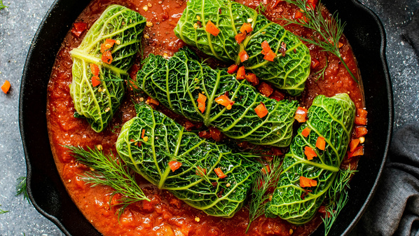 KI generiert: Grüne Kohlrouladen in einer roten Soße, garniert mit Kräutern und Paprika in einer Pfanne.