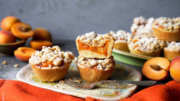 KI generiert: Kleine Aprikosen-Streuselkuchen auf einem Teller, dekoriert mit Halbiertem.