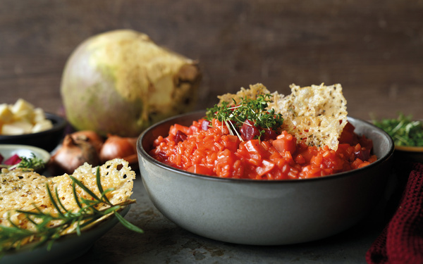 KI generiert: Eine Schüssel mit rotem Eintopf, dekoriert mit Kräutern und Käsechips. Im Hintergrund Gemüse.