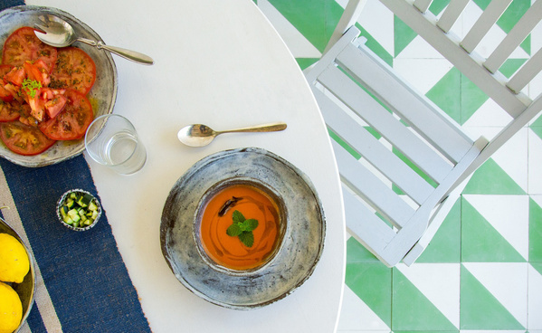 KI generiert: Eine Tischszene mit Tomatensalat, Suppe, Getränk und Zitrone auf weißem und grünem Fliesenboden.