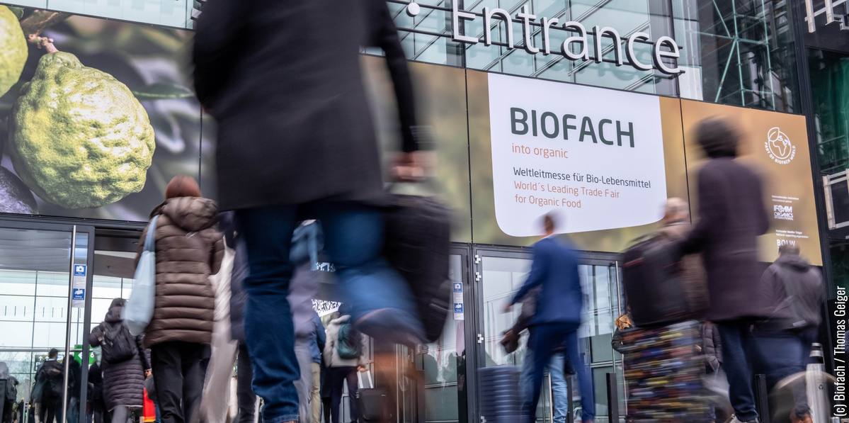 KI generiert: Menschen betreten eine Messe mit dem Schild: „BIOFACH - Weltleitmesse für Bio-Lebensmittel“.