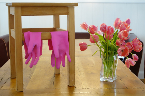 Pinke Handschuhe über einem Hocker, daneben ein Strauß Tulpen