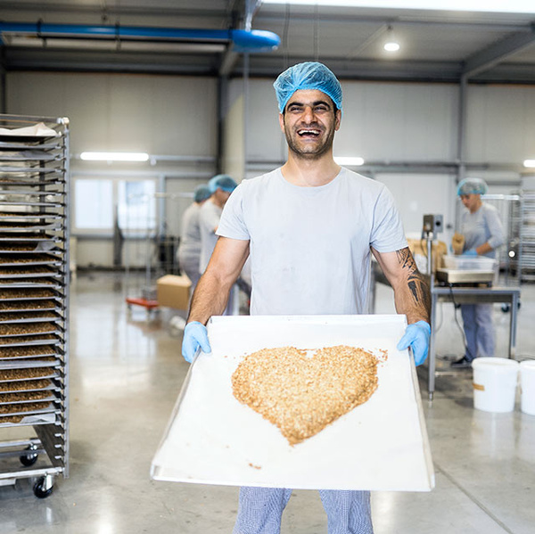 Grünland Bio Lieferant Heyho Mitarbeiter mit Granola-Herz auf Backblech