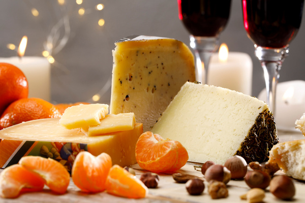 KI generiert: Käseplatte mit Mandarinen, Nüssen, Kerzen und Rotweingläsern im Hintergrund.