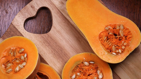Das Bild zeigt geschnittene Butternut-Kürbisse auf einem Holzbrett mit herzförmigem Ausschnitt. Die leuchtend orangefarbene Farbe des Kürbisfleischs und die sichtbaren Kerne sind prominent.