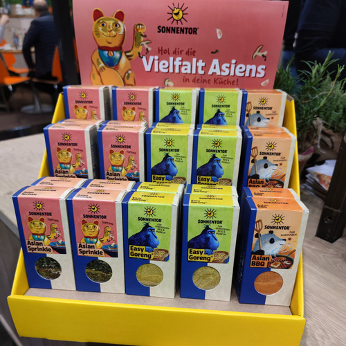 KI generiert: Ein Gewürzdisplay von Sonnentor mit verschiedenen asiatischen Gewürzmischungen. Text: "Hol dir die Vielfalt Asiens in deine Küche!"