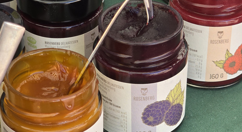 KI generiert: Drei Gläser Marmelade auf einem Tisch, Beschriftung "Rosenberg Delikatessen".