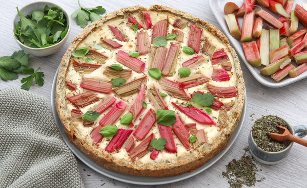 KI generiert: Eine herzhafte Tarte mit Rhabarberstücken, grünem Blattdekor und Kräutern garniert.