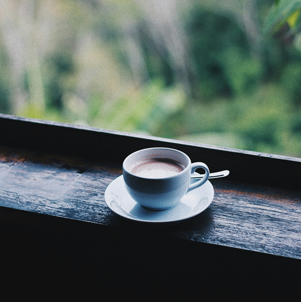 KI generiert: Weiße Tasse mit Kaffee auf einer Fensterbank vor einer grünen, verschwommenen Landschaft.