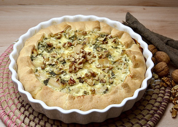 KI generiert: Quiche mit Walnüssen in einer runden Form auf geflochtener Unterlage.