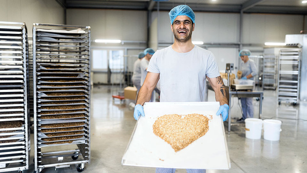 Mitarbeiter von HEYHO! präsentiert geröstetes Granola in Herzform auf Backblech