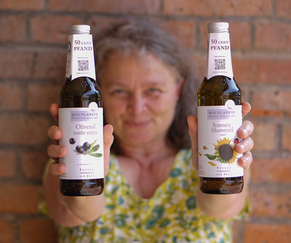 KI generiert: Eine Person hält zwei Flaschen Bio-Öl: Olivenöl und Sonnenblumenöl. Text: "BIO PLANÈTE, Olivenöl, Sonnenblumenöl".