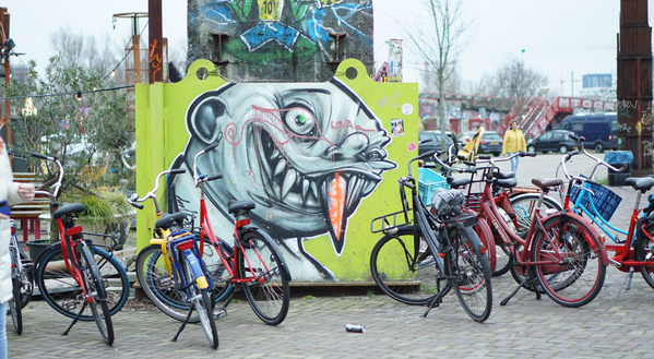 Streetart-Graffiti Glatzkopf mit spitzen Zähnen  an einer Wand, davor Fahrräder geparkt