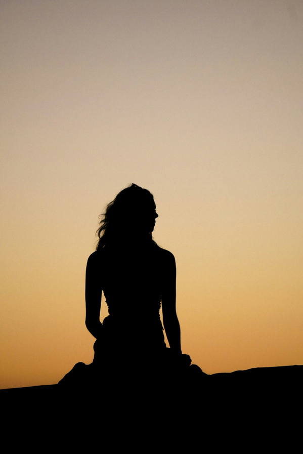 KI generiert: Eine Silhouette einer Person sitzt vor einem Sonnenuntergang.
