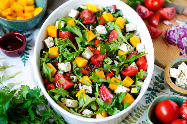 KI generiert: Ein bunter Salat in einer Schüssel, bestehend aus Tomaten, Mango, Feta und Rucola.