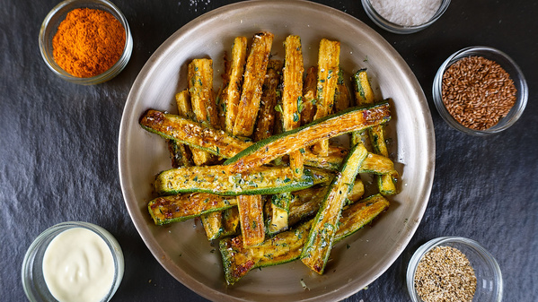 Ein Teller gebratene Zucchinistreifen, umgeben von Gewürzen und Dips.