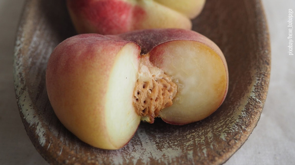 Flachpfirsich angeschnitten in patinierter ovaler Holzschale