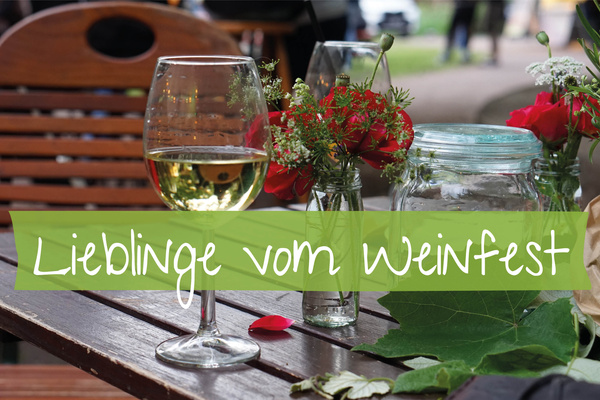 KI generiert: Weinglas und Blumen auf einem Tisch. Text: "Lieblinge vom Weinfest".