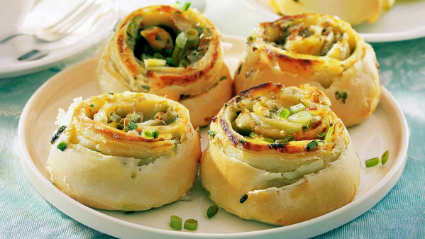 KI generiert: Vier herzhafte Teigschnecken mit Frühlingszwiebeln auf einem weißen Teller serviert.