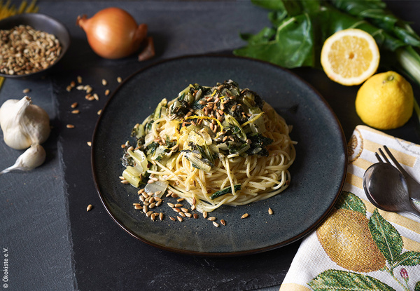 KI generiert: Ein Teller Spaghetti mit einer Gemüse-Sauce, umgeben von Zwiebel, Zitrone und Knoblauch, dekoriert mit Samen.