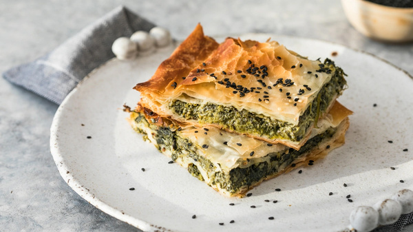 KI generiert: Zwei Stücke Spinat-Filo-Pastete auf einem Teller, bestreut mit schwarzen Sesamsamen.
