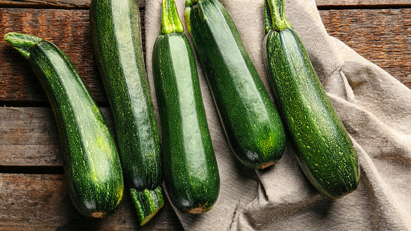 KI generiert: Fünf grüne Zucchini liegen auf einem Holztisch und einem Leinentuch.