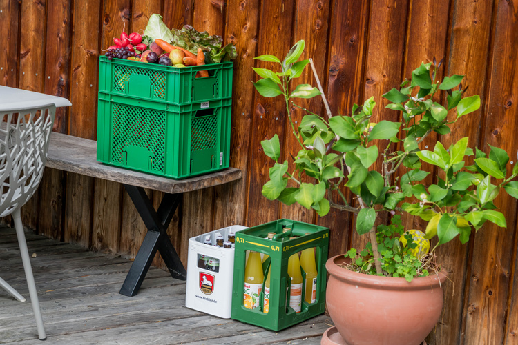 KI generiert: Kisten mit Gemüse und Getränken, daneben eine Pflanze auf einer Terrasse.