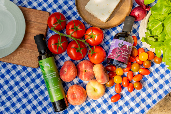 Strauchtomaten, Flachpfirsiche, Cherrytomaten mit Produkten Aroma Olymp auf blaukarierter Tischdecke