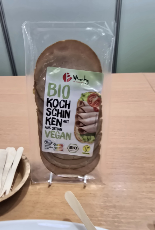 KI generiert: Vegane Wurst aus Seitan in Bio-Verpackung auf einem Tisch. Text: "BIO KOCHSCHINKEN ART AUS SEITAN VEGAN".