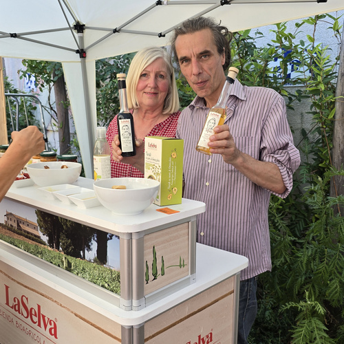 KI generiert: Zwei Personen präsentieren Produkte an einem Stand; LaSelva-Logo und Getränkeflaschen sind sichtbar.