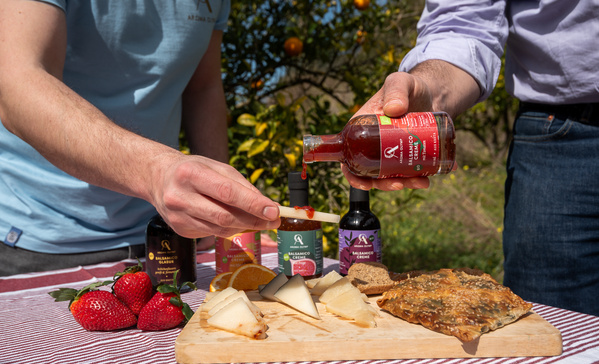 KI generiert: Picknick mit Käse, Erdbeeren und Balsamico. Hände halten Essensartikel.