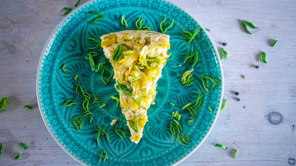 Ein Stück Lauch-Quiche auf einem blauen Teller, dekoriert mit Frühlingszwiebelstücken.