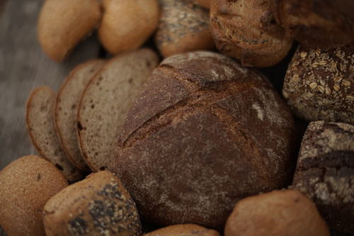 KI generiert: Verschiedene Brotsorten, darunter ein Laib Roggenbrot, geschnittenes Brot und Brötchen.