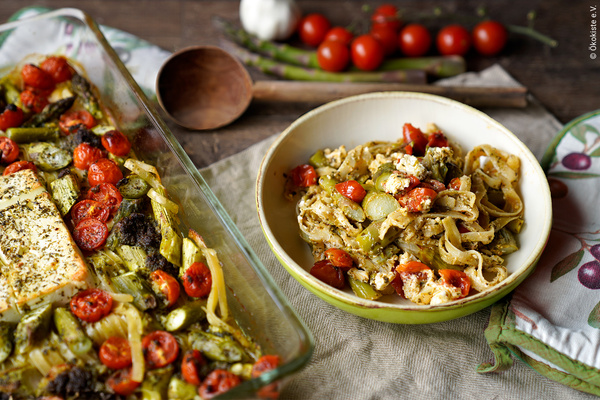 KI generiert: Ein Gericht mit gebackenem Gemüse, Feta und Tomaten in einer Auflaufform und einer Schüssel. Text: "© Ökokiste e.V."