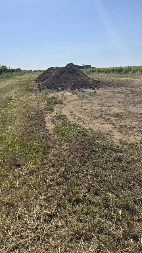 KI generiert: Ein großer Haufen Erde auf einem Feld unter klarem Himmel.