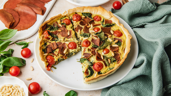 Eine Gemüsequiche mit Tomaten, Spinat und veganem Belag auf einem weißen Teller