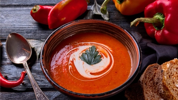 KI generiert: Eine Schüssel Paprikasuppe mit Sahne und Petersilie, umgeben von frischen Paprika und Brot.