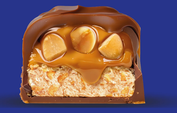Querschnitt von einem Schoko-Erdnuss-Karamell-Riegel in Nahaufnahme vor blauem Hintergrund