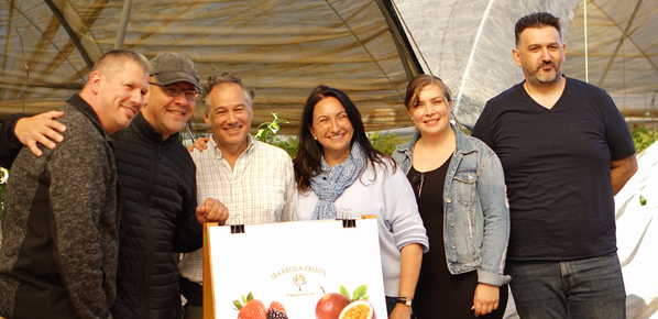 KI generiert: Eine Gruppe von sechs Personen posiert lächelnd vor einem Plakat mit Früchten. Text: "IBARROLA FRUITS".
