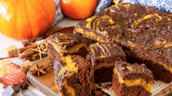 KI generiert: Kürbis-Schokoladen-Kuchenwürfel auf einem Holzbrett, dekoriert mit Kürbissen und Herbstblättern.