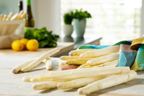 WEißer Spargel in ein Küchentuch eingeschlagen, im Hintergrund Zitronen und frische Kräuter