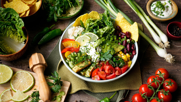 Ein bunter Salat mit Gemüse, Bohnen, Tortilla-Chips und Limette. Links Limettenscheiben, oben frische Kräuter.