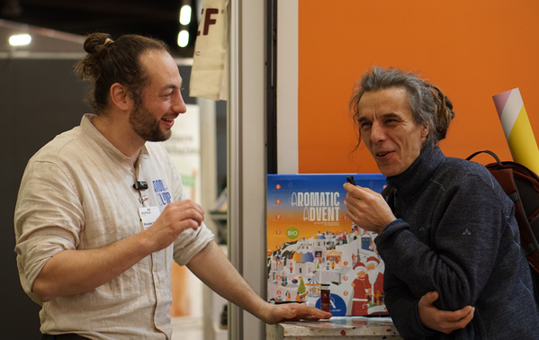 KI generiert: Zwei Männer unterhalten sich vor einem "Aromatic Advent"-Kalender.