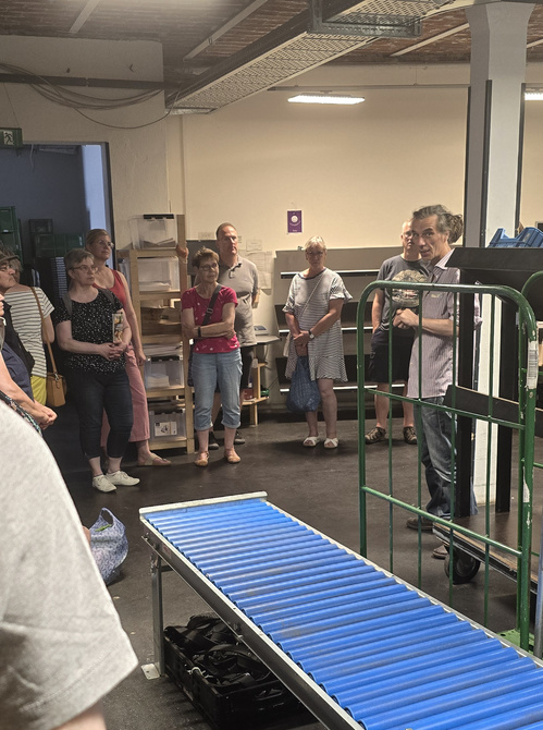 KI generiert: Eine Person spricht zu einer Gruppe von Menschen in einem Lagerraum.